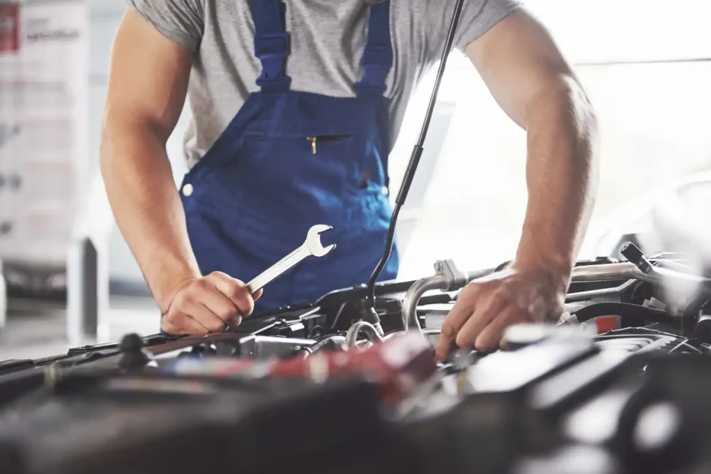 Auto mechanic in blue overalls repairing a car engine with a wrench in a workshop, lemonlawassist
