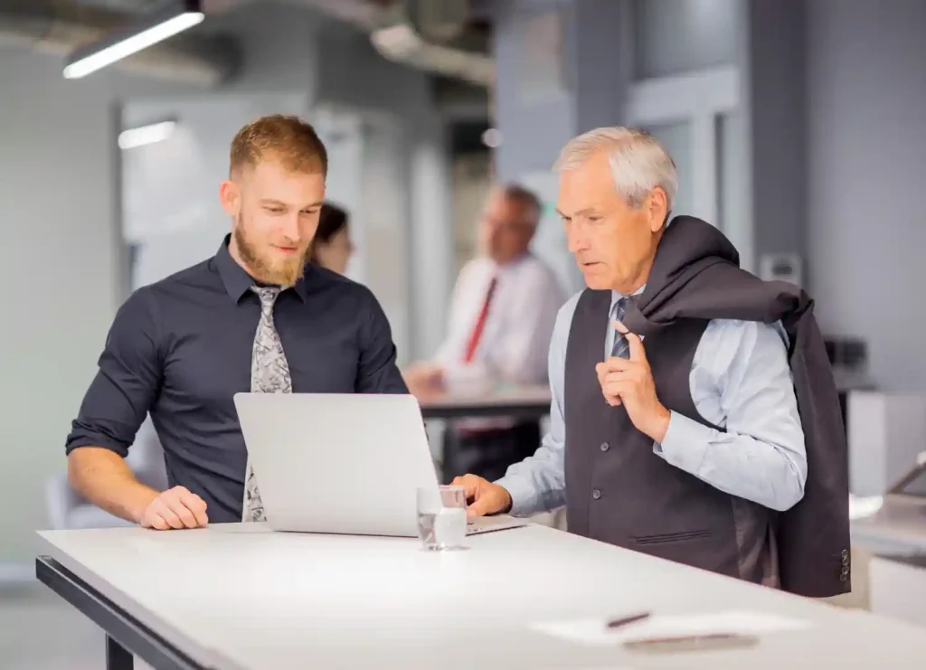 Two person standing near the table looking at laptop in the office