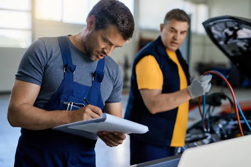 mechanic writing on clipboard while repairing car engine