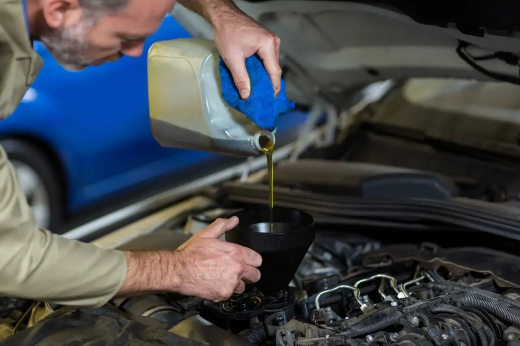 Mechanic pouring oil into car engine, lemonlawassist
