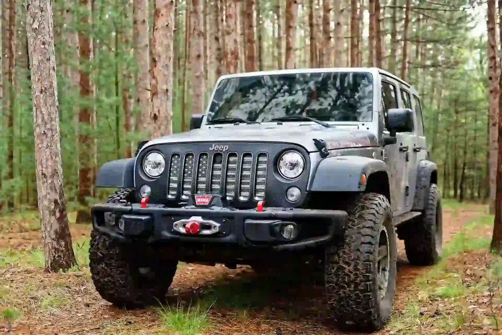 An off-road-ready black Jeep Wrangler, equipped with rugged tires and a front winch, parked in a forest setting.