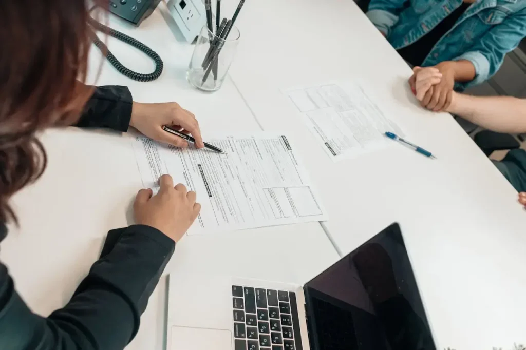 The image depicts formal setting, where a person is seen filling out forms on a white desk. The individual holds a pen and is focused on the paperwork.