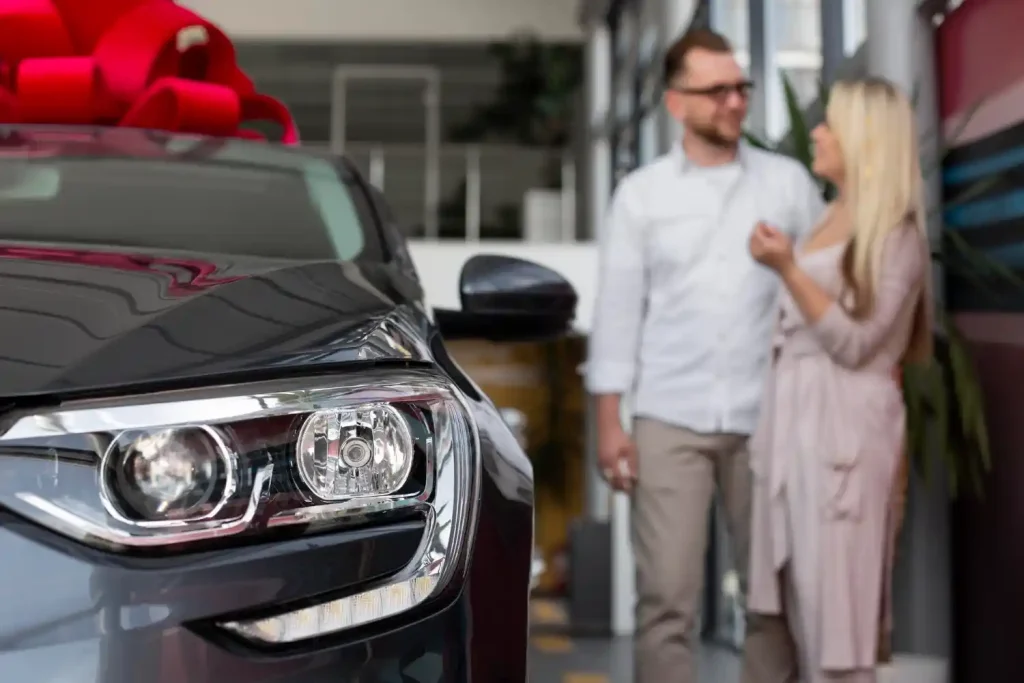 Close-up of a new car with a red bow, while a happy couple, lemonlawassist