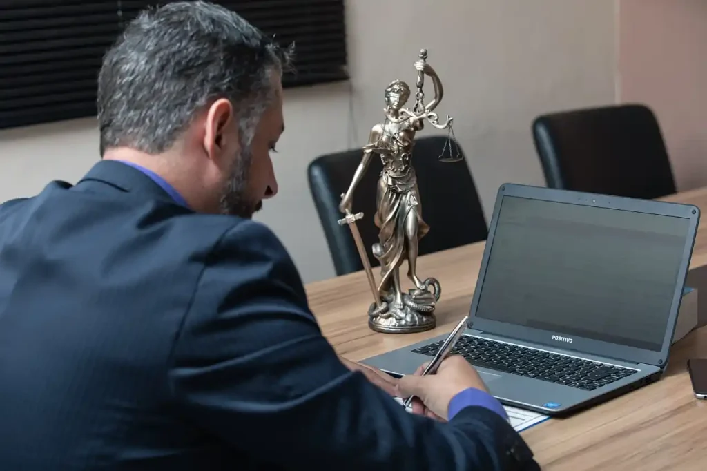 Lawyer working at a desk with a laptop and Lady Justice statue, symbolizing legal services and justice, lemonlawassist
