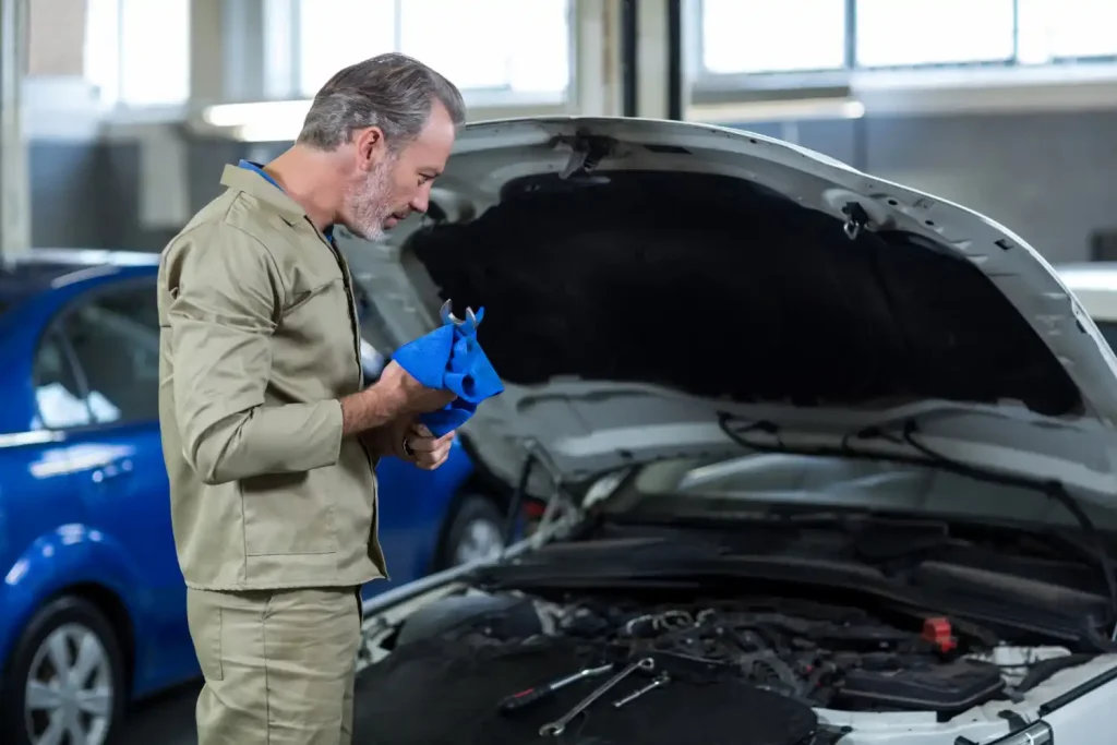 Mechanic inspecting a car engine with tools laid out on the vehicle, in a workshop setting, lemonlawassist