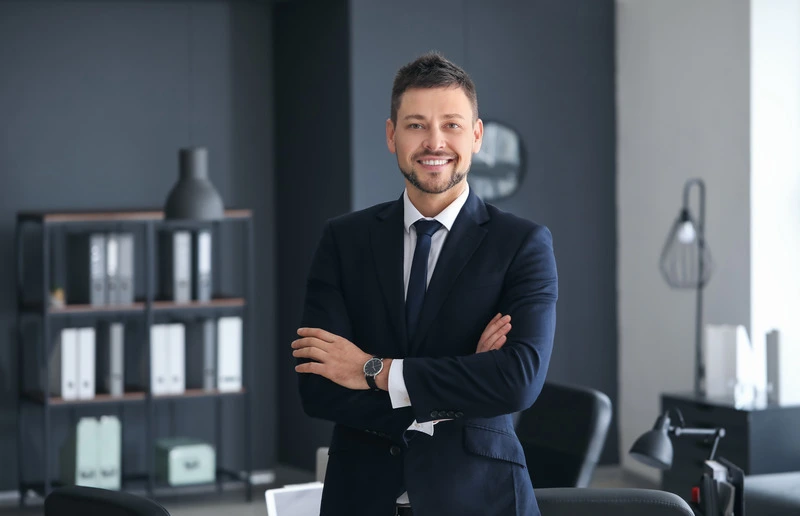 Smiling lawyer professional in modern office, wearing a suit and crossing arms confidently, lemonlawassist