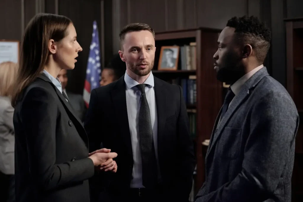 Three attorney professionals engaged in a serious discussion in a formal setting, lemonlawassist