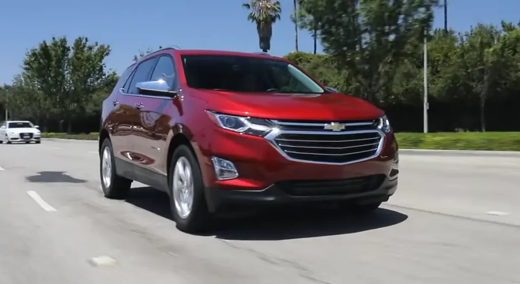 A red Chevrolet Equinox SUV driving on a sunny road with trees and other vehicles in the background, lemonlawassist
