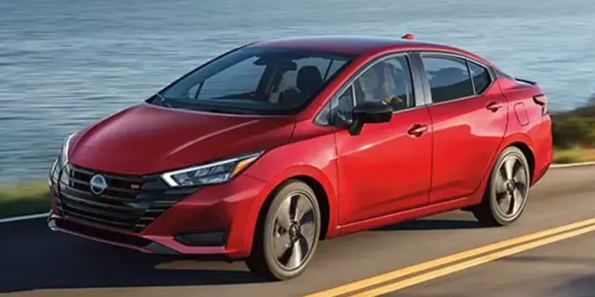 A sleek red Nissan sedan driving along a scenic coastal road, with water visible in the background, lemonlawassist