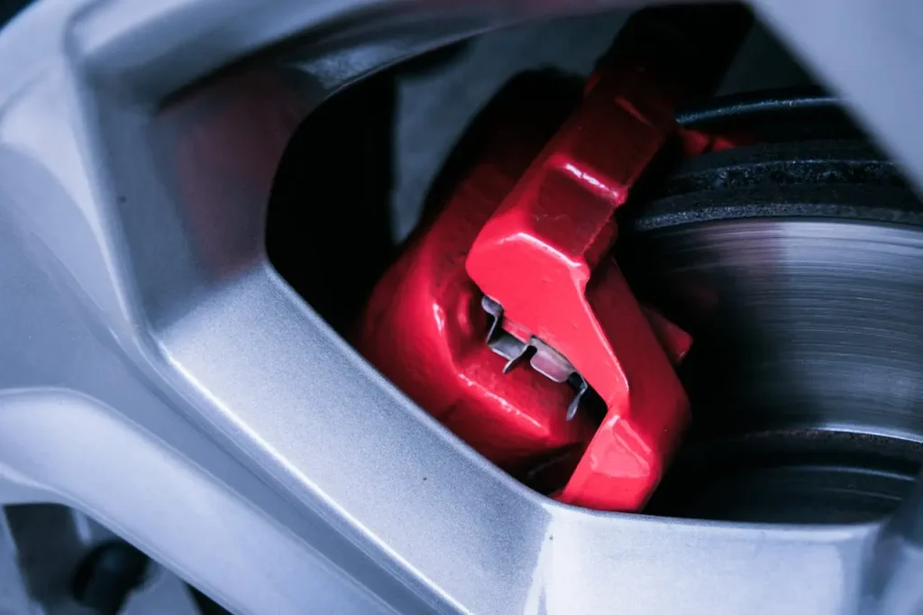 Close-up of a bright red car brake caliper inside a silver alloy wheel, showcasing automotive detail and engineering, lemonlawassist