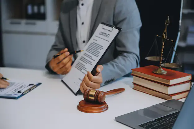 Lawyer in a suit holding a contract during a consultation, with gavel, justice scales, lemonlawassist
