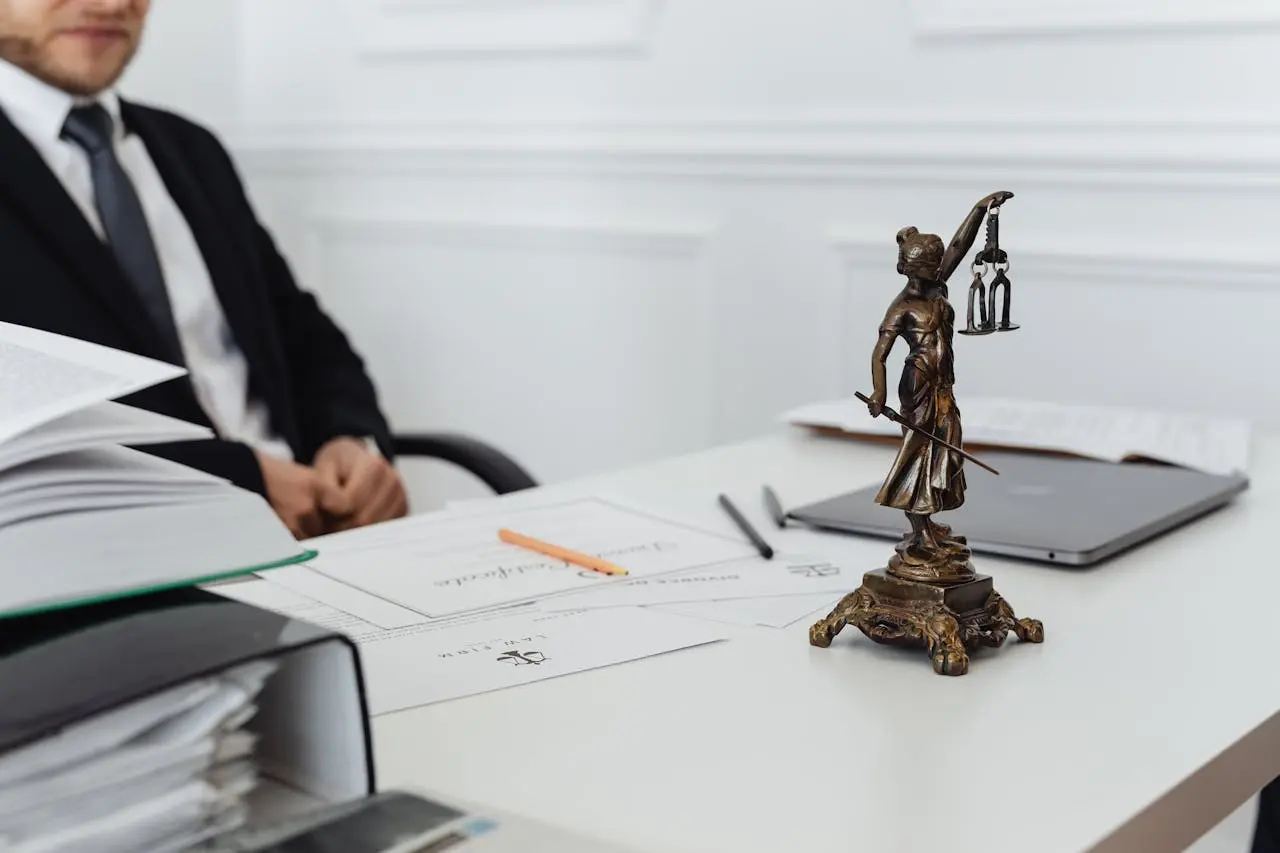 Lawyer in a suit sitting at a desk with Lady Justice statue, documents, lemonlawassist