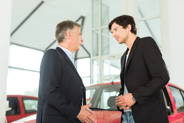 Mature car dealer discussing vehicle options with a young man in a car dealership showroom, lemonlawassist