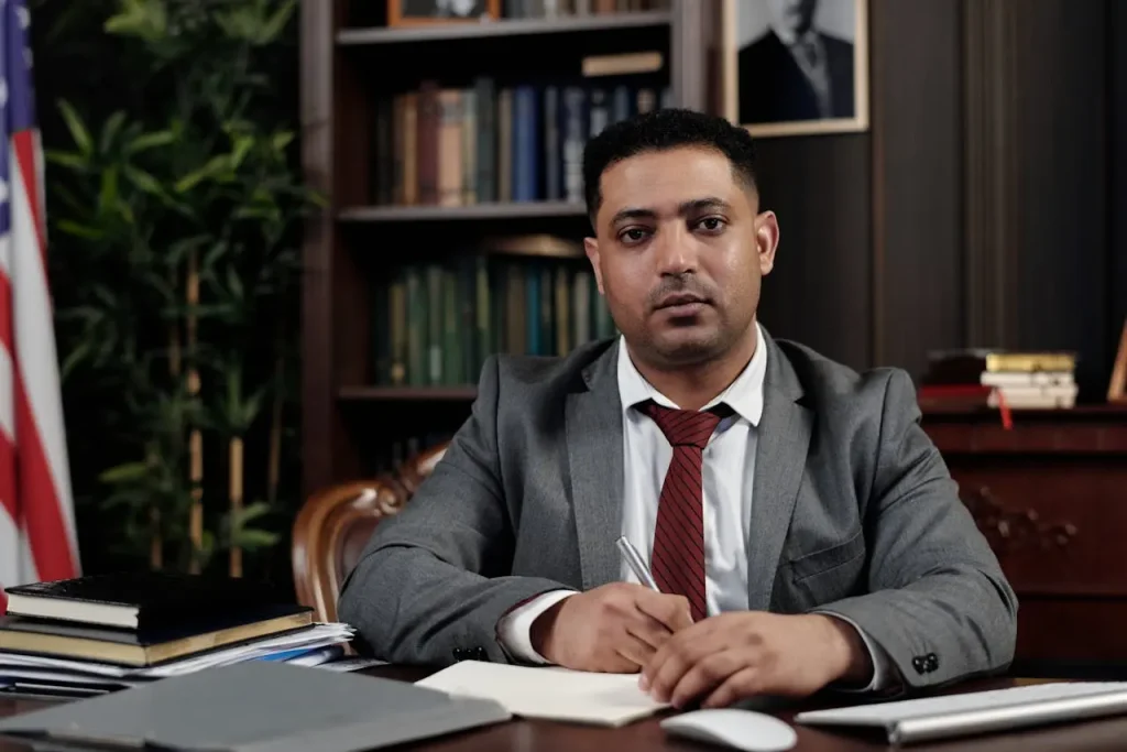 A professional lawyer in a suit and tie seated at a desk with books, papers, and a computer mouse, lemonlawassist
