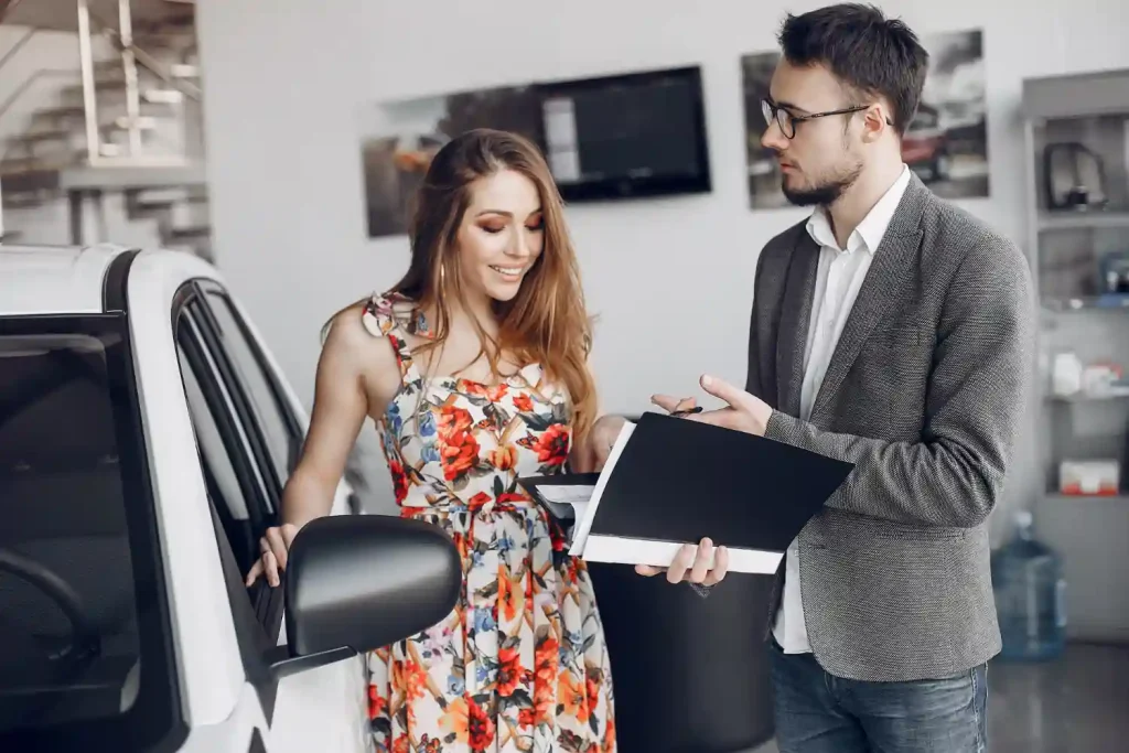 A woman in a colorful floral dress smiles while talking to a man in a blazer holding a black folder, lemonlawassist