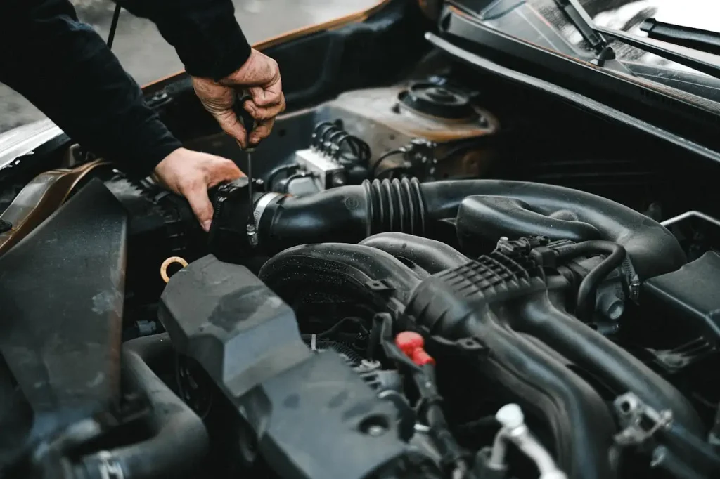Close-up of a mechanic’s hands working on a car engine, using a screwdriver to adjust components under the hood of a vehicle, lemonlawassist