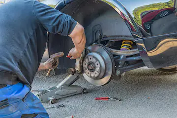 Mechanic working on a car brake system, using tools while the vehicle is elevated on a jack, lemonlawassist