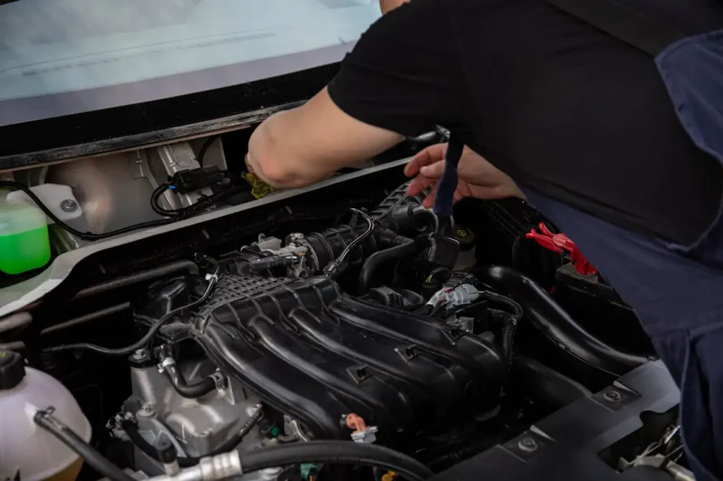 A mechanic in a black shirt works on a car engine, inspecting and adjusting components under the hood, lemonlawassist