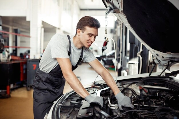 Auto mechanic inspecting a car engine in a professional repair shop, wearing gloves and overalls, focused on vehicle maintenance, lemonlawassist