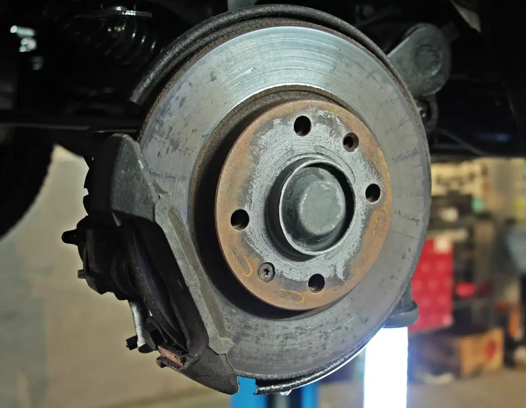 Close-up view of a car's brake disc and caliper in a workshop setting, showcasing the mechanical details of the braking system, lemonlawassist
