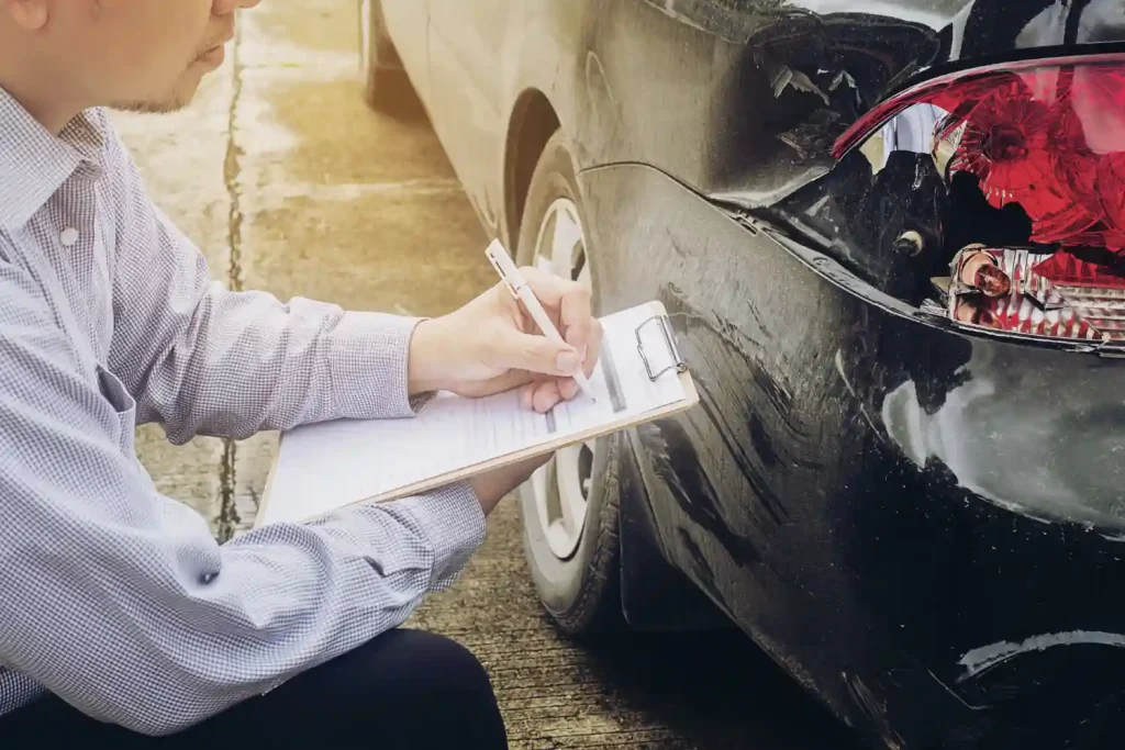 Inspecting a damaged car with a clipboard, documenting details of the accident for assessment and claims processing, lemonlawassist