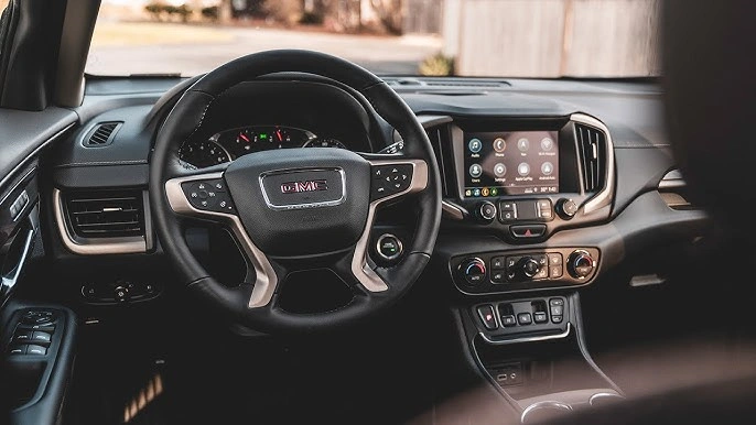 Interior view of a GMC vehicle focusing on the steering wheel, dashboard, and infotainment system, showcasing modern controls and sleek design, lemonlawassist