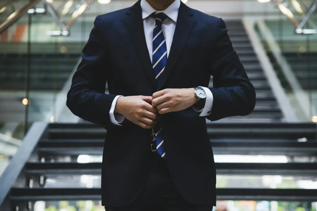 Lawyer in a formal dark suit with a striped tie, adjusting his jacket while standing on stairs inside a modern building with glass railings, lemonlawassist