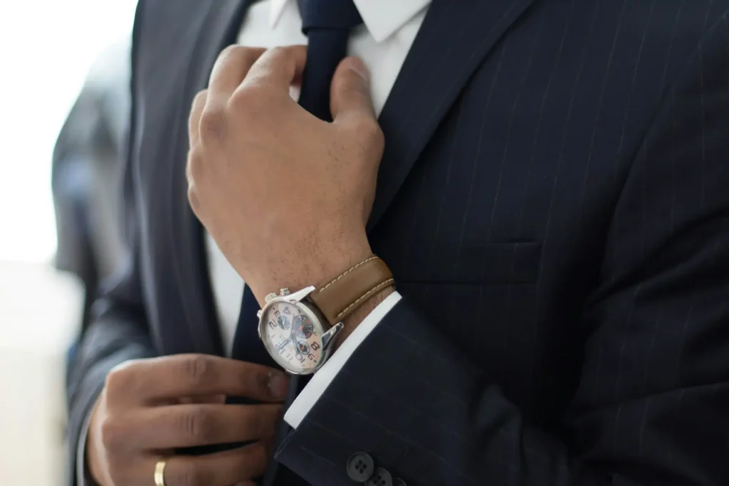 Close-up of a lawyer in a dark pinstriped suit adjusting his tie, with a tan leather-strap wristwatch visible on his wrist, exuding professionalism and style, lemonlawassist