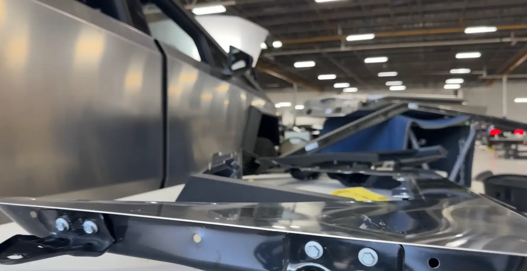 Close-up view of a Tesla Cybertruck inside a workshop or factory, with metal components and structural parts laid out in the foreground, lemonlawassist