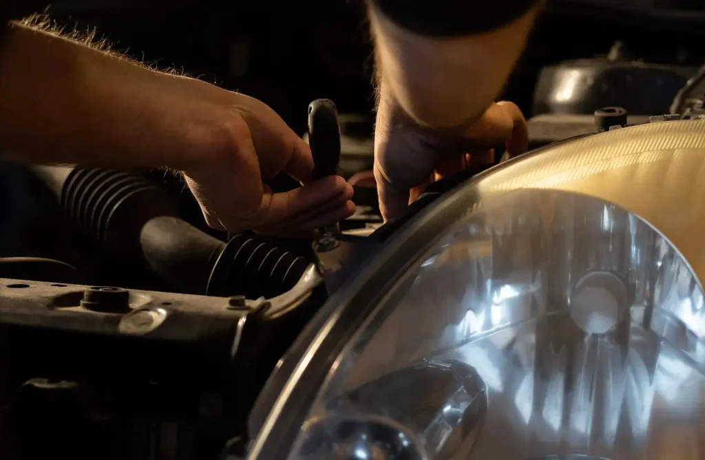 Mechanic using a tool to repair a car engine near the headlight, lemonlawassist