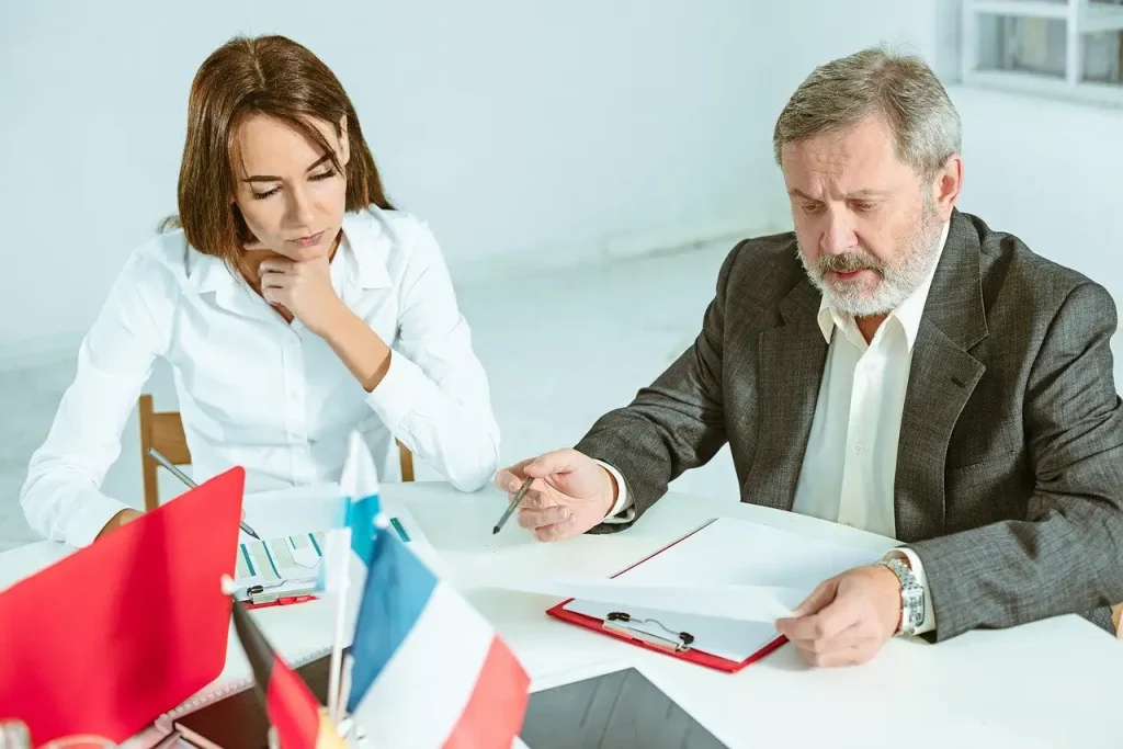 Two lawyers professionals in discussion at a meeting table with documents, flags, and a laptop, lemonlawassist