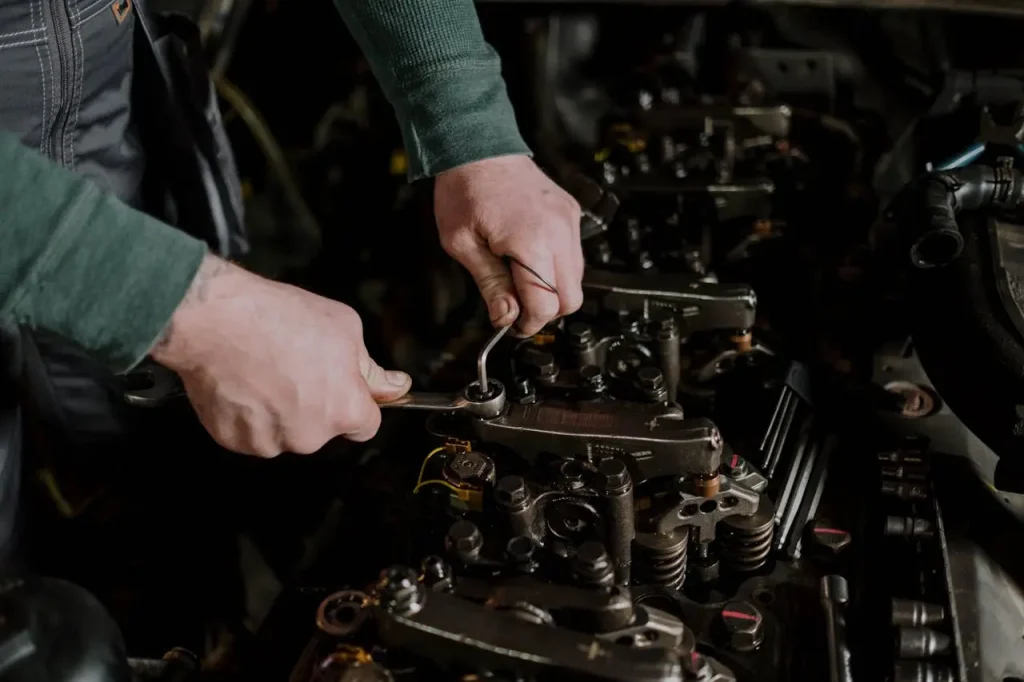 A mechanic using tools to perform maintenance on a car engine, focusing on detailed engine components, lemonlawassist