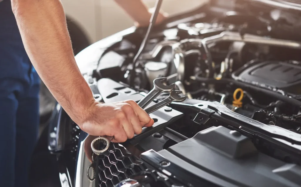 Auto mechanic holding wrenches while inspecting a car engine in a repair shop, lemonlawassist