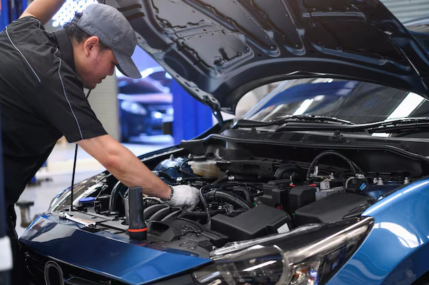 Auto mechanic inspecting a car engine in a repair shop, diagnosing a breakdown issue under the hood of a blue vehicle, lemonlawassit