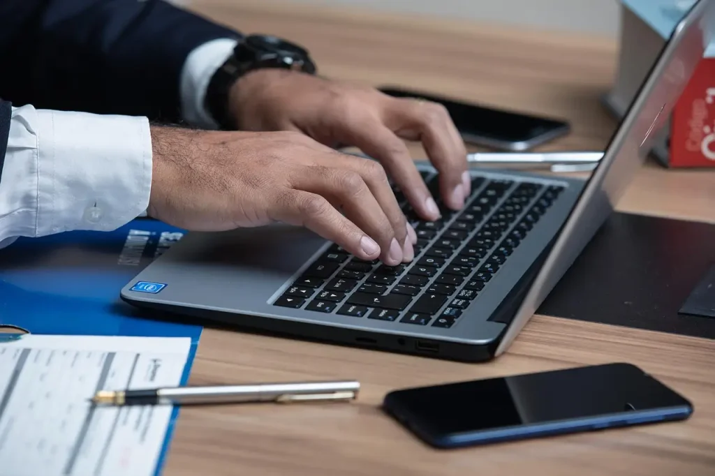 Lawyer typing on a laptop at a desk with documents, pen, and smartphone, lemonlawassist