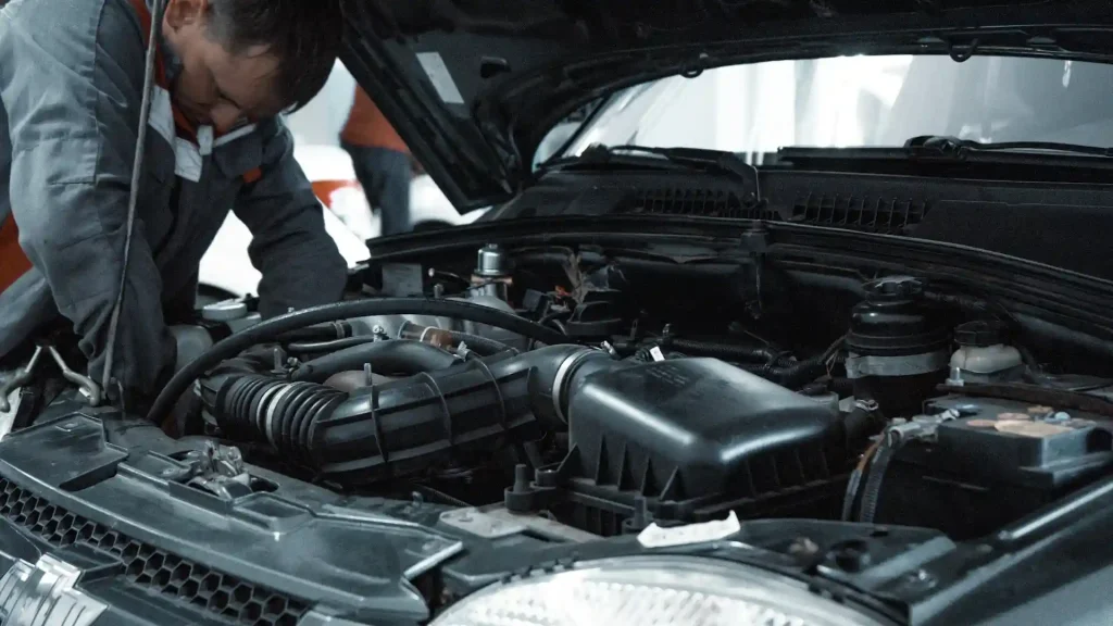 Auto mechanic inspecting a car engine under the hood in a repair shop, lemonlawassist