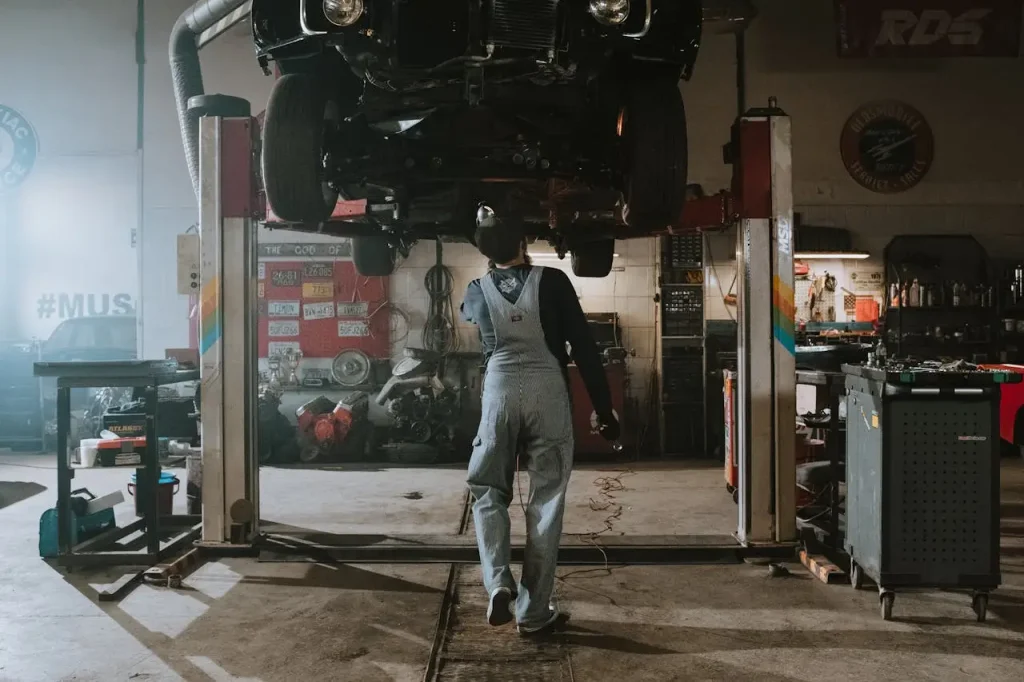 Auto mechanic inspecting the underside of a car lifted in a professional garage setting, lemonlawassist
