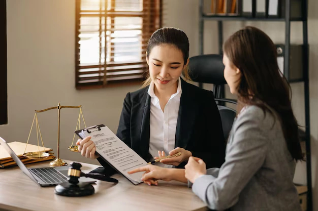 Female lawyer explaining contract terms to client in legal office with gavel and scales of justice on desk, lemonlawassist