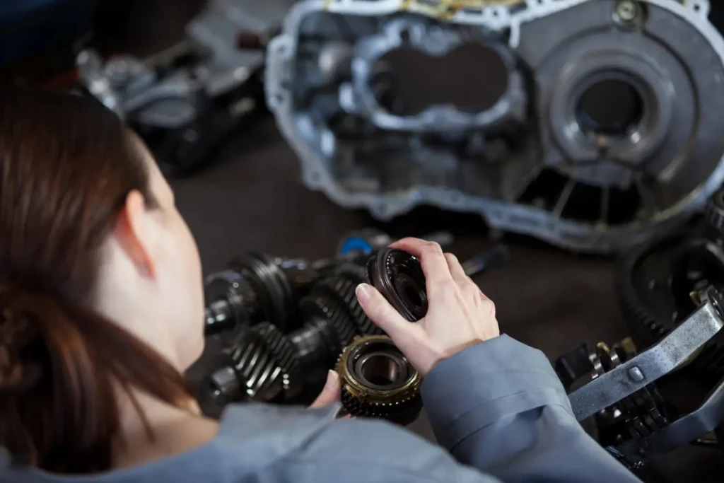 Female mechanic inspecting automotive gears during transmission repair in a workshop, lemonlawassist