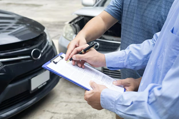 Insurance agent assisting driver with paperwork after a car accident involving two vehicles, lemonlawassist