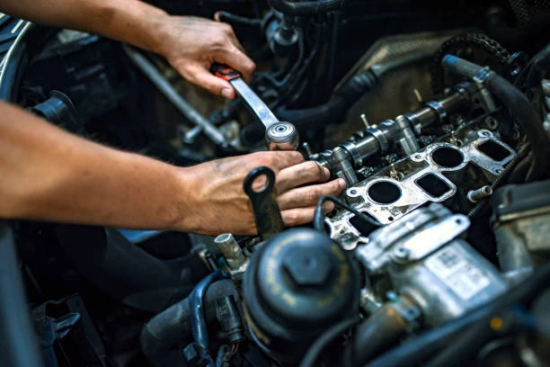Mechanic using wrench to repair engine components inside car hood, lemonlawassist