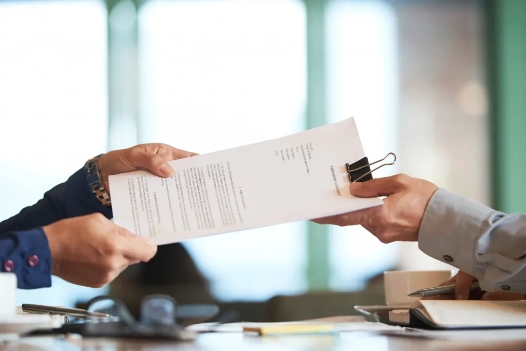 Two lawyer professionals exchanging a contract or legal document at a desk, lemonlawassist