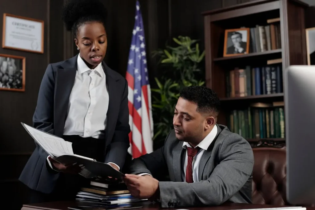 Two lawyers reviewing documents in a law office with bookshelves and a U.S. flag in the background, lemonlawassist