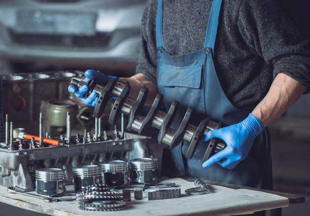Auto mechanic handling a crankshaft with blue gloves in an engine rebuild workshop, lemonlawassist