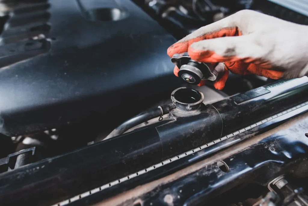 Mechanic’s gloved hand opening a car radiator cap during engine inspection, lemonlawassist